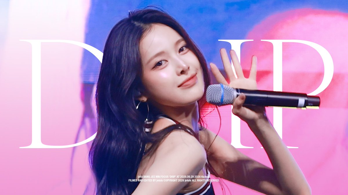 A performance photo of K-pop idol Jang Jee Min at a 'FOCUS 'DRIP'' fan event, waving while holding a microphone against a pink and blue backdrop with 'DDP' lettering; text credits 'FILMED AND EDITED by jehlu' with a 2026 copyright.