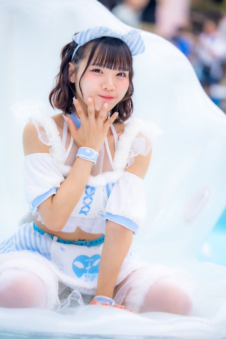 A young woman in a white and blue maid-style outfit with striped accents poses playfully, showing off her outfit details and accessories.