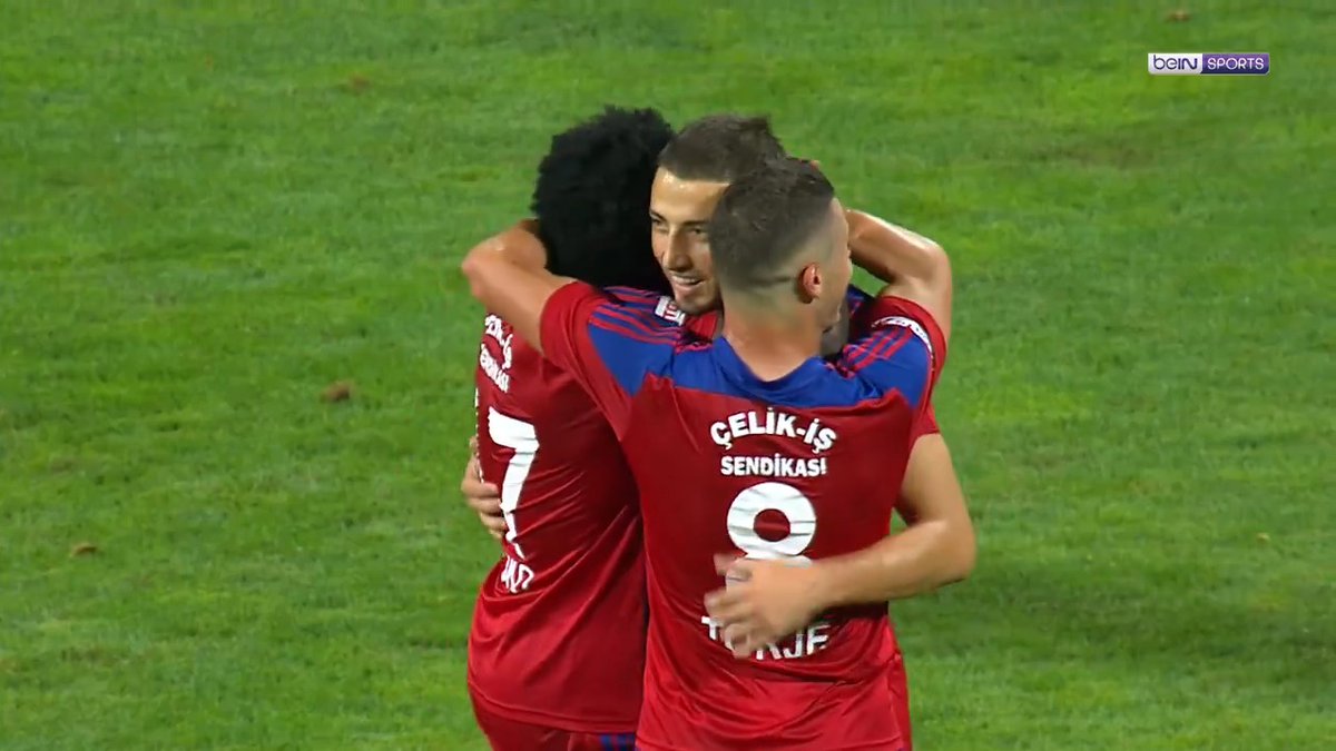 Gheorghe Grozav, wearing jersey number 9, hugs his Karagümrük teammates in red kits after scoring from distance on the beIN SPORTS broadcast.
