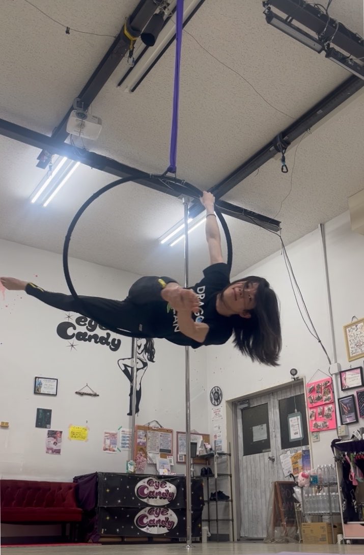A woman performing on an aerial hoop (lyra) hanging from the ceiling in a studio with 'Eye Candy' branding visible on the walls.