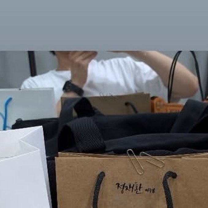 A blurry image shows a person in a white shirt sitting behind a cardboard box with black handles and Korean text '강제소환 명단' written on it.