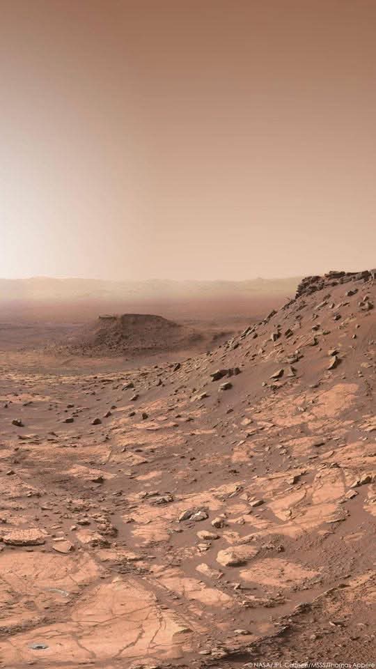 konstructivizm's tweet photo. Gale Crater, Through Curiosity’s Eyes

Two years ago, NASA’s Curiosity rover paused in Gale Crater and looked back across a landscape that feels almost impossible: a dry, sculpted world of layered hills, wind-carved ridges, and ancient lakebed stone — all under a thin Martian sky.

In the distance, the crater rim rises like a far-off mountain wall, a reminder that this entire scene sits inside a giant impact basin some 154 kilometers across. What looks like quiet desert was once a place of water, sediment, and time stacked in stone.

These are natural colors — not a painter’s flourish, but the rust, gold, and muted blue-gray that Curiosity actually saw.

Credit: NASA