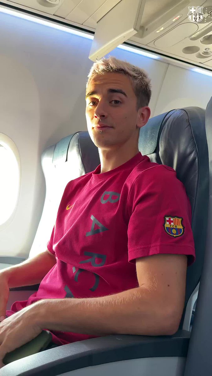 A young man with bleached blonde hair sits on an airplane wearing a maroon FC Barcelona t-shirt featuring the club's crest, with the team's logo watermark in the corner. The image likely accompanies a social media post teasing an unexpected but exciting pairing of players or teammates traveling together.