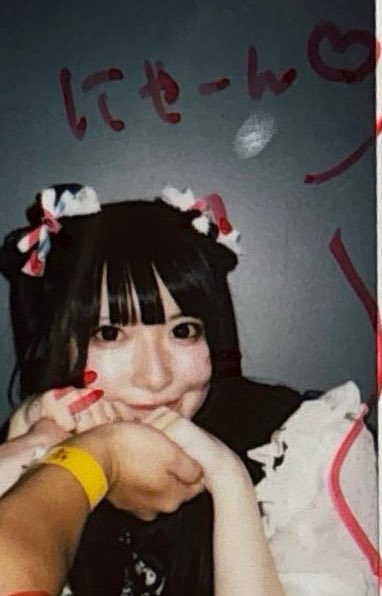 A selfie of a woman with dark hair wearing decorative hair bows, posing with her hands near her face; Japanese text 'にゃーん' with a heart is written above her.