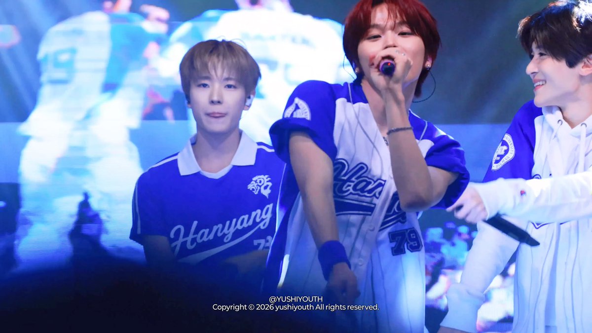 Three performers on stage in blue and white 'Hanyang' baseball-style jerseys, with the center figure singing into a microphone, watermarked '@YUSHIYOUTH Copyright © 2026 yushiyouth All rights reserved.'