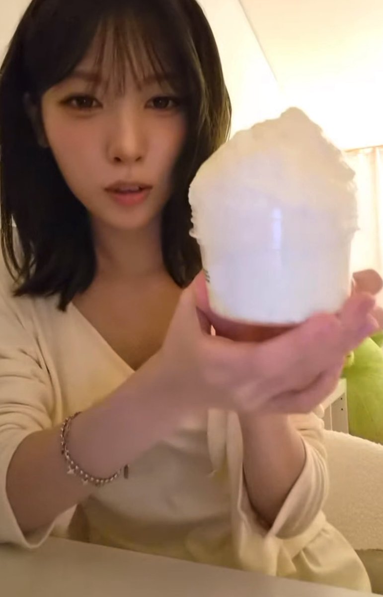A young woman with dark shoulder-length hair holds up a large cup of cotton candy while wearing a cream-colored top and a beaded bracelet.