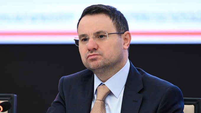 A bespectacled man in a dark suit, light blue shirt, and golden-orange tie sits in what appears to be a conference setting with red and white banners blurred in the background. The image accompanies a Turkish caption declaring "Mr. Akın Gürlek is Our Red Line! This Nation Stands Behind Him and Will Continue To!"—framing him as a figure of strong public support.