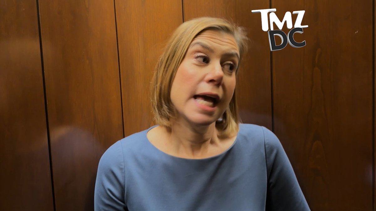 A blonde woman in a blue dress speaks animatedly while standing in front of wood-paneled walls, with a "TMZ DC" logo visible in the top right corner of the frame.