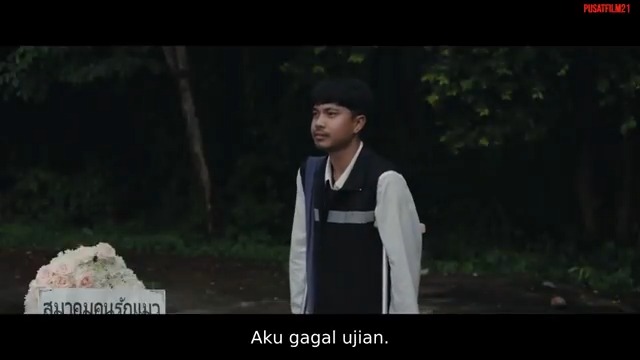 Still from a Thai film showing a young man in a school vest standing in a dark forest near a tombstone, with subtitles reading 'Aku gagal ujian.'