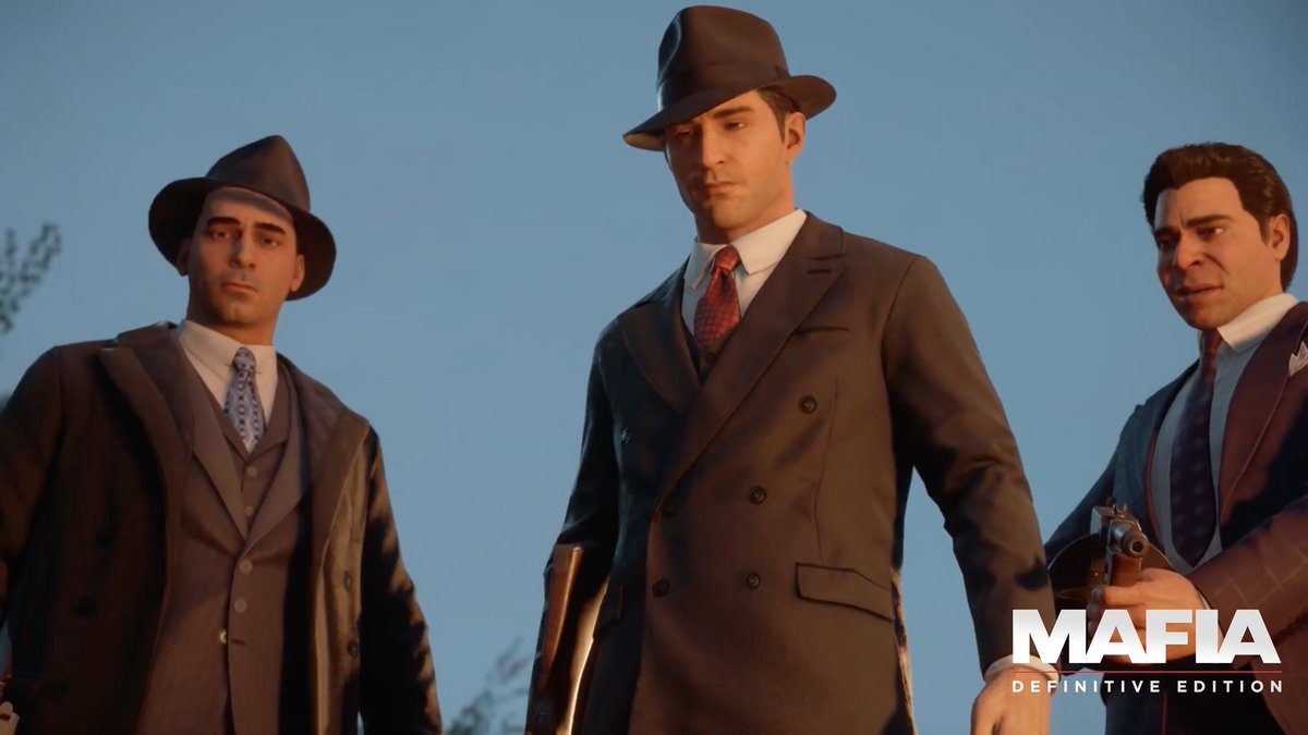 Three men in 1930s-style suits and fedoras stand against a dusky sky, with the central figure in a double-breasted coat flanked by armed associates, including one holding a pistol on the right. The "Mafia: Definitive Edition" logo appears in the bottom right corner, tying the scene to the game's Prohibition-era mob setting.