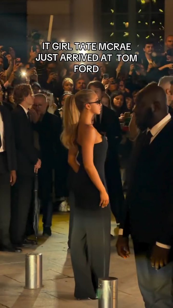A blonde woman in a black outfit walks past a crowd of photographers and security guards, with text reading 'IT GIRL TATE MCRAE JUST ARRIVED AT TOM FORD' overlaid.
