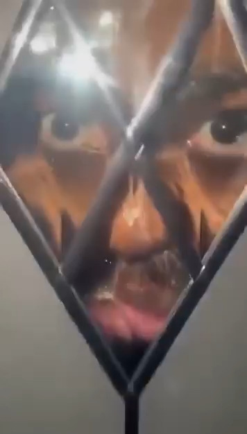 A close-up image where the reflection of their face appears within the triangular geometric design of the surface.