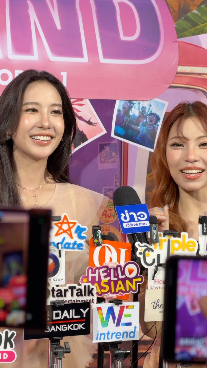 Two smiling women with dark and reddish-brown hair pose at a press event behind a cluster of media microphones including 'ข่าวสด', 'HELLO ASIAN', 'StarTalk entertainment', 'DAILY BANGKOK', and 'WE in trend'.