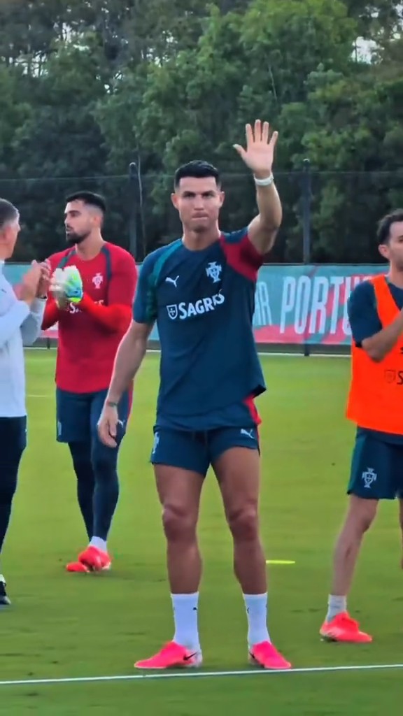 Cristiano Ronaldo, wearing a Portugal training kit with "SAGRES" printed across the chest, waves to fans on a training pitch alongside teammates applauding him, capturing a heartfelt tribute to his career. The "PORTUGAL" banner in the background underscores the national team's farewell gesture for the legendary footballer.