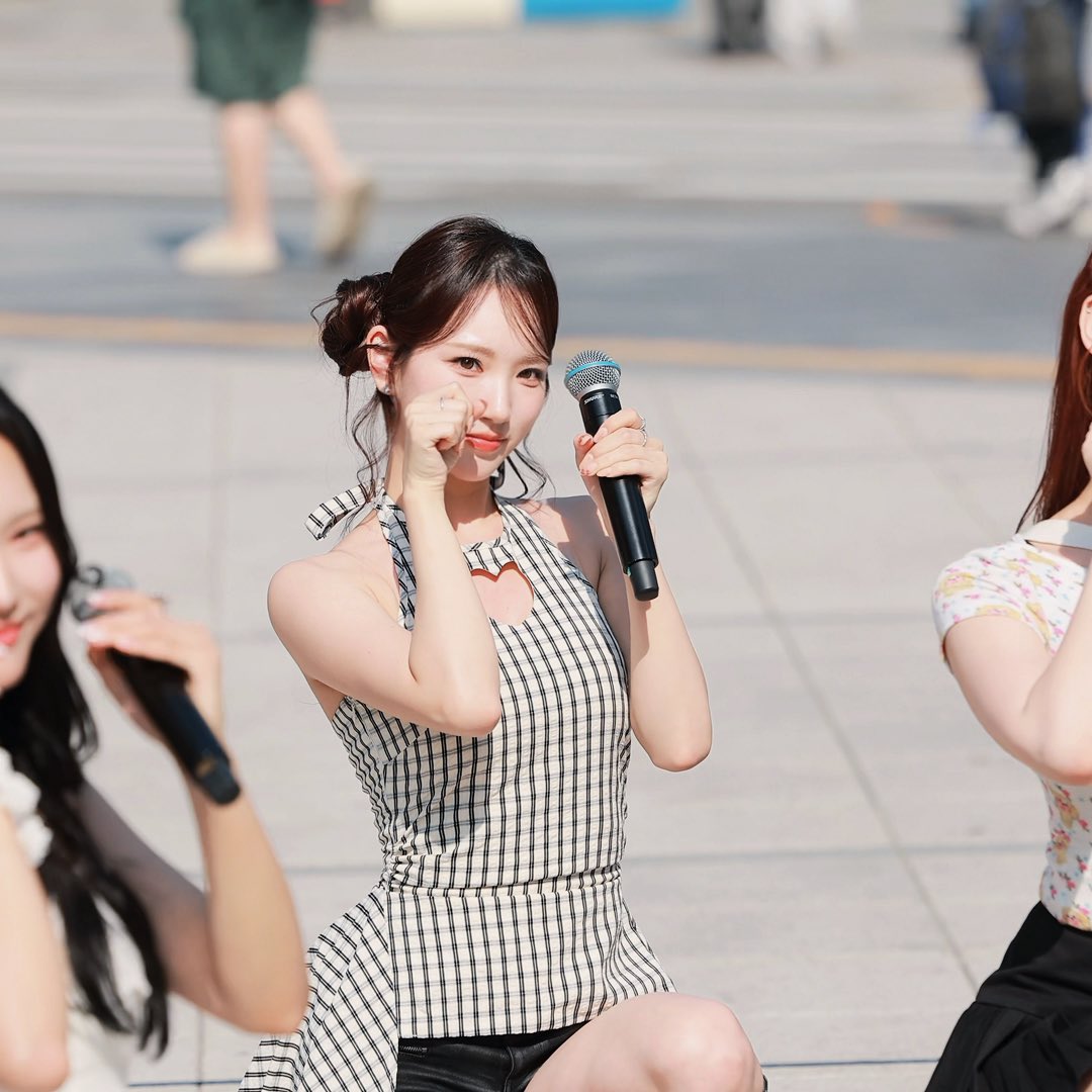 A woman in a checkered halter dress holds a microphone while posing outdoors.