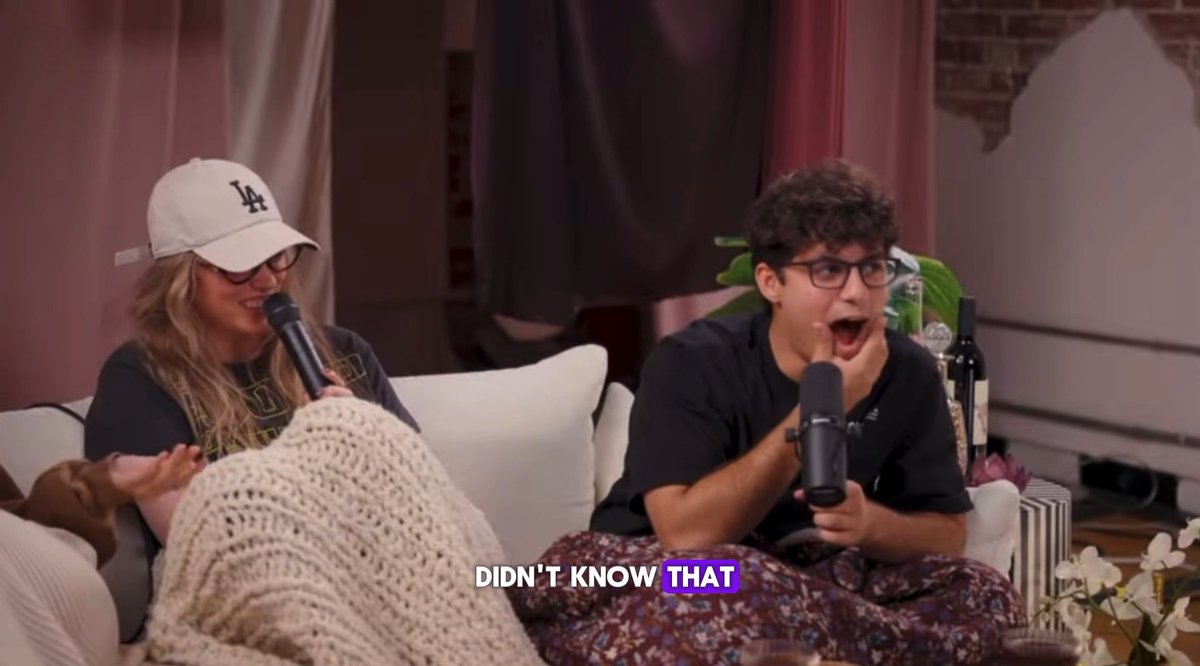 Two people are seated on a couch holding microphones, with the woman on the left wearing an LA baseball cap and glasses, and the young man on the right reacting with a shocked expression; the text 'DIDN'T KNOW THAT' appears at the bottom.