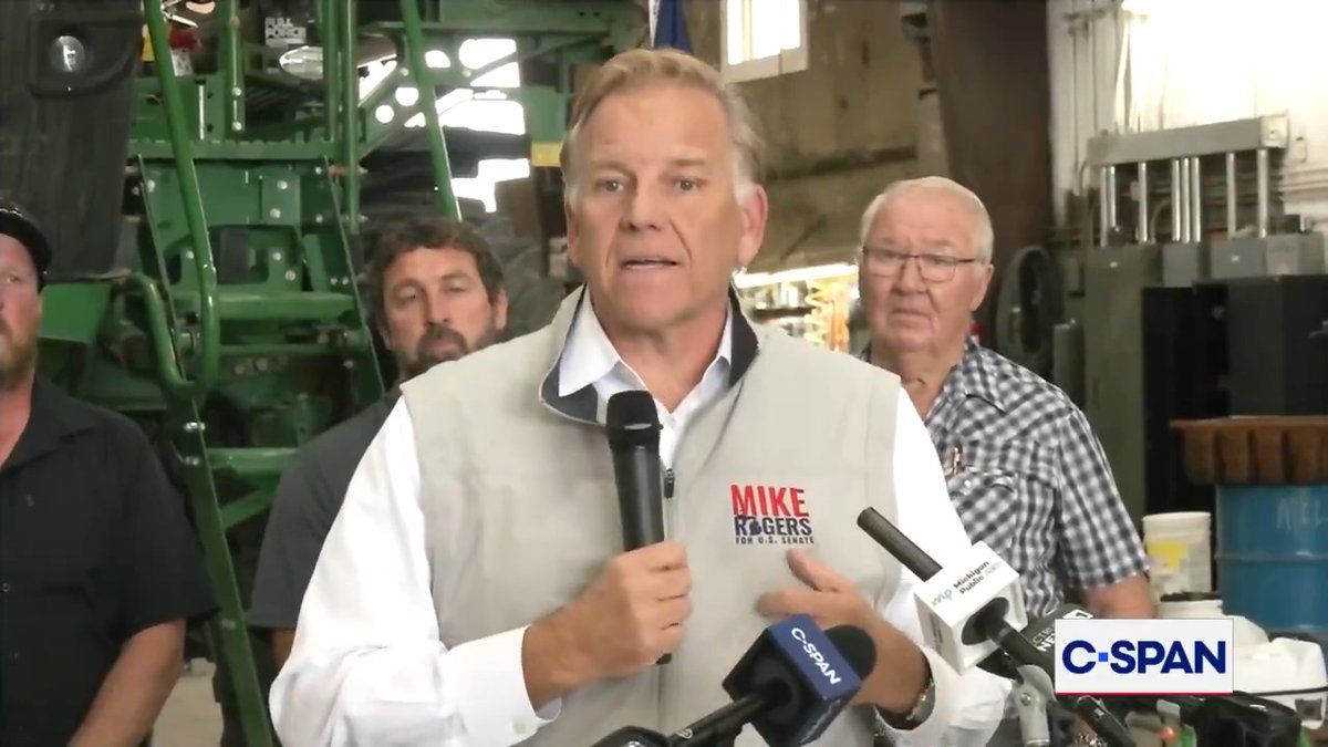 Mike Rogers, candidate for U.S. Senate, speaking into multiple microphones at a C-SPAN event in what appears to be a barn or agricultural facility.