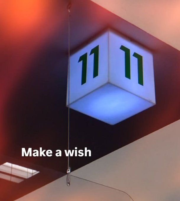 An illuminated cube lamp hanging from the ceiling displays the number "11 11" in green, with the text "Make a wish" overlaid on the image.