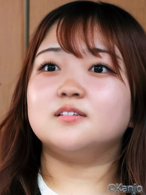 A close-up portrait of a young woman with long reddish-brown hair and bangs, looking directly at the camera with a neutral expression; the watermark '©Kanjo' is visible in the bottom right corner.