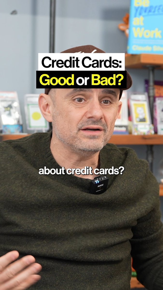 A screenshot from a video featuring a man in a brown cap and green sweater with a Rode microphone, overlaid with text reading 'Credit Cards: Good or Bad?' and 'about credit cards?' with a book titled 'Be More at Work' visible behind him.