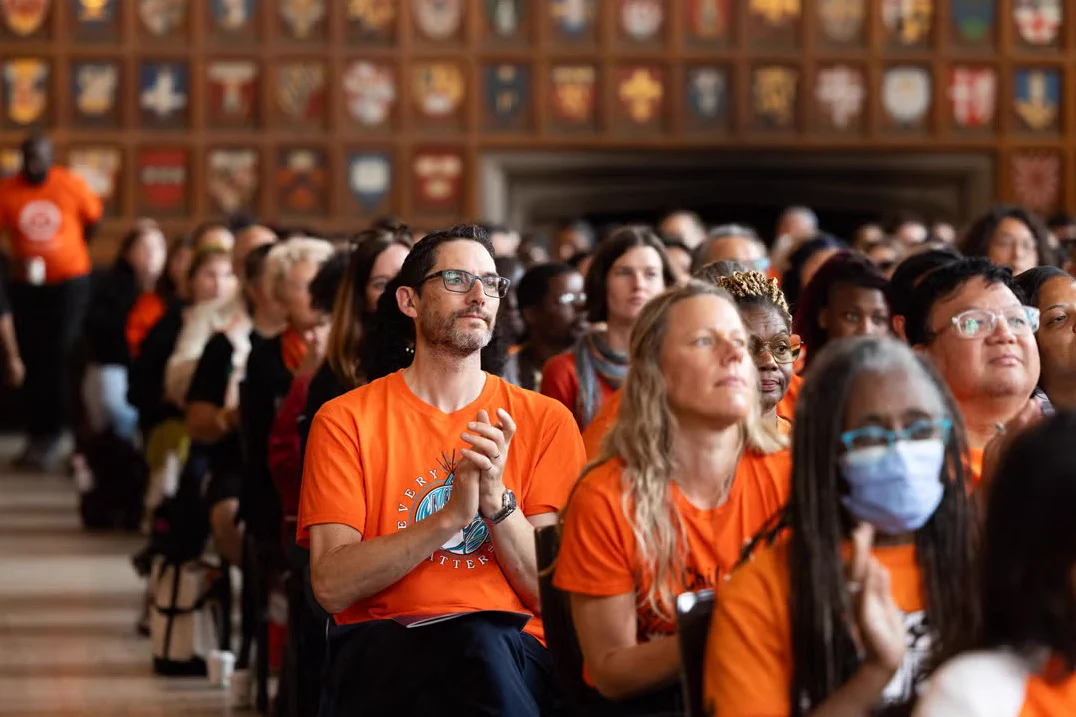 A group of people sitting in an audience wearing orange shirts