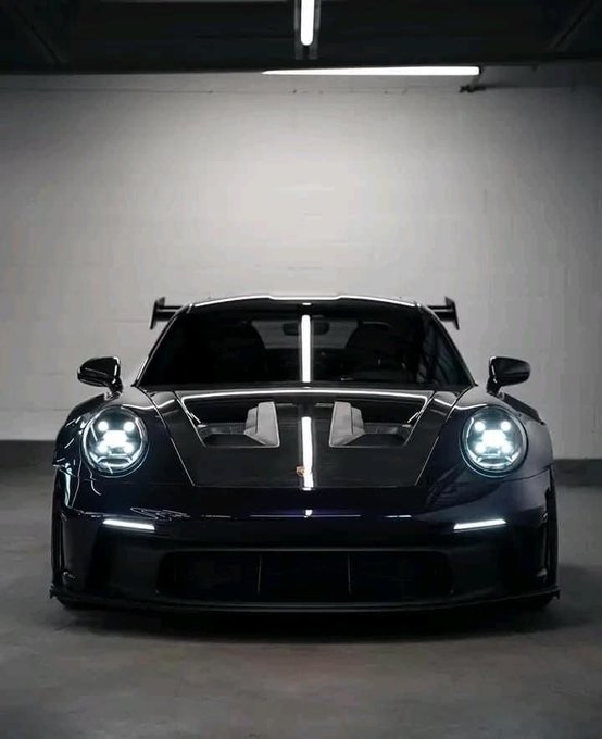 A sleek black Porsche 911 GT3 with a prominent rear wing sits in a dimly lit garage, its headlights glowing beneath an overhead light, capturing the menacing aesthetic implied by the caption "those."