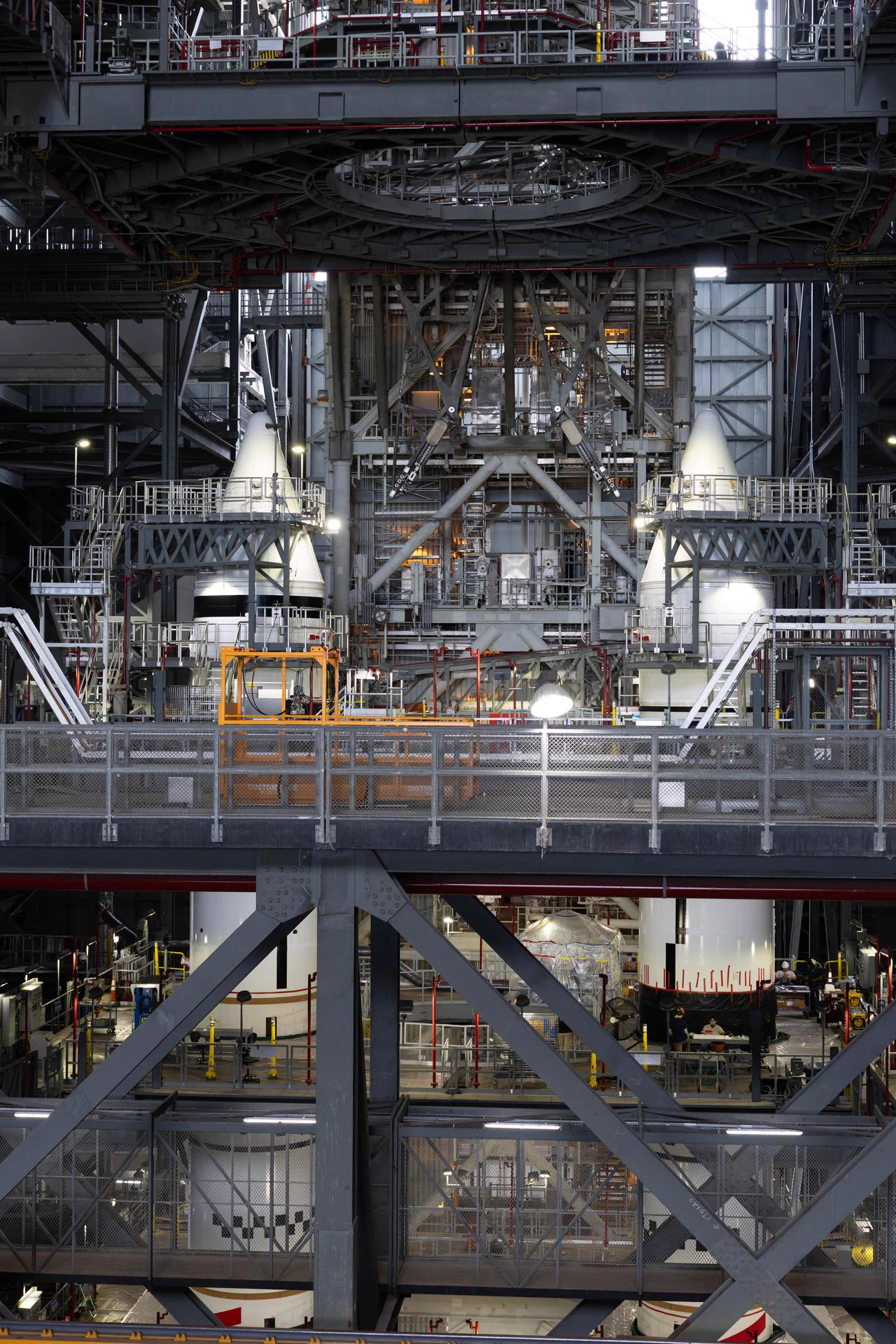Two towering, fully stacked white SLS solid rocket boosters rise inside the massive Vehicle Assembly Building, surrounded by scaffolding as teams prepare them for Artemis III. Credit: NASA/Cory S. Huston