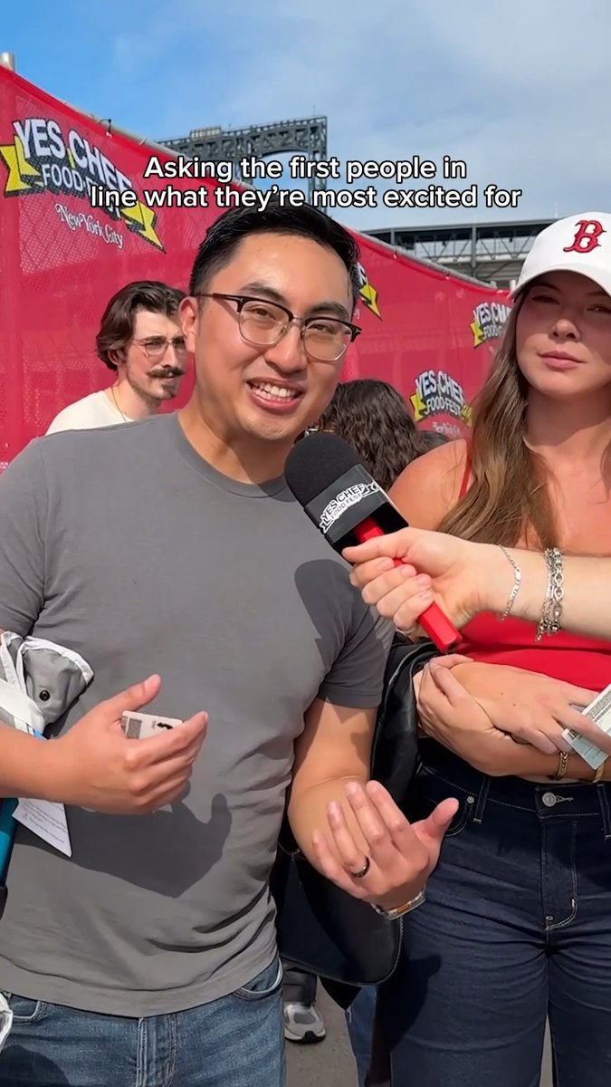 A man being interviewed by someone holding a 'Yes Chef Food Fest' microphone, with on-screen text reading 'Asking the first people in line what they're most excited for' at the New York City event.