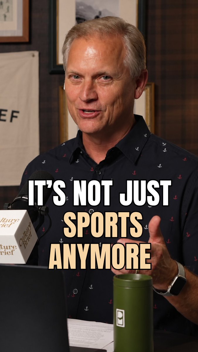 A man in a navy anchor-pattern shirt speaks at a podium with overlaid text reading 'IT'S NOT JUST SPORTS ANYMORE'.