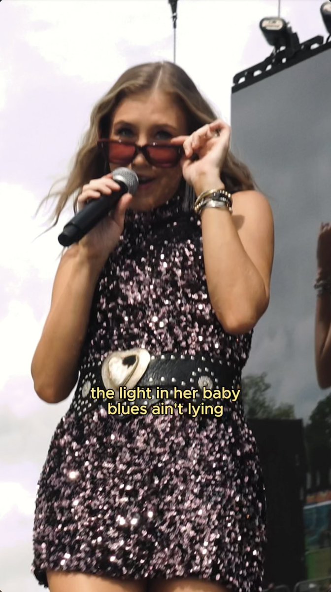 A performer in a sparkly sequined dress singing into a microphone while holding red sunglasses, with text overlay 'the light in her baby blues ain't lying'.