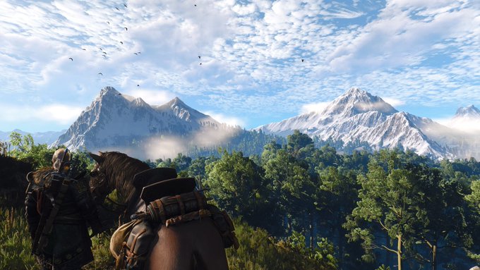 A scenic landscape from a video game showing a character on horseback overlooking a vast valley with snow-capped mountains in the distance.