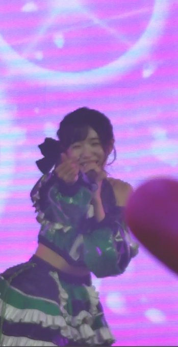 A performer in a green and white outfit sings into a pink microphone on a brightly lit stage with pink lighting.