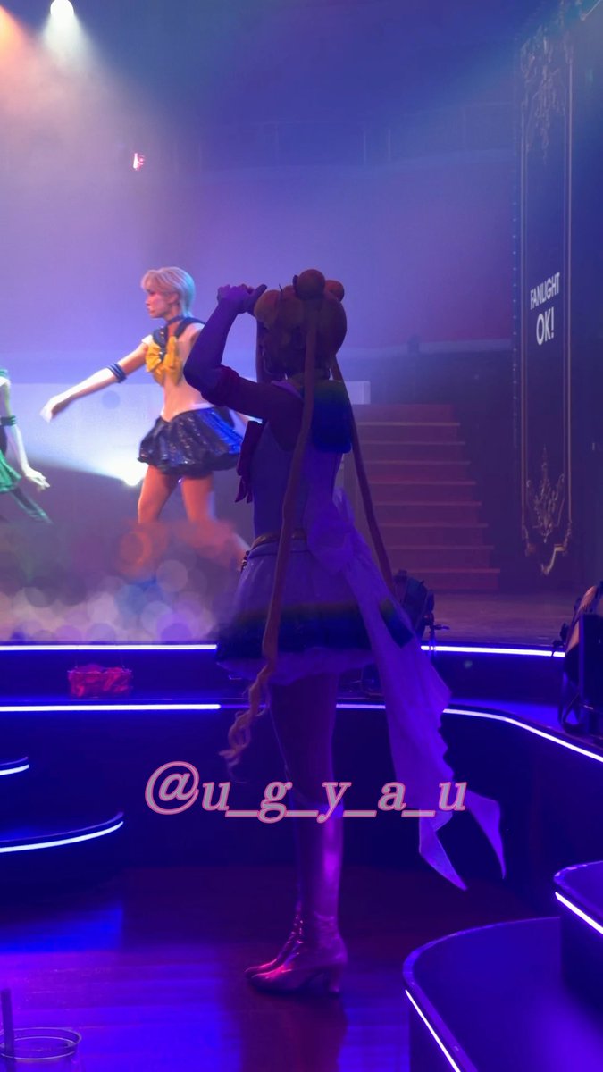 An idol performance scene with a cosplayer in purple outfit facing a large screen displaying an anime Sailor Moon character, with 'FINALIGHT OK!' visible and watermark @u_g_y_a_u.