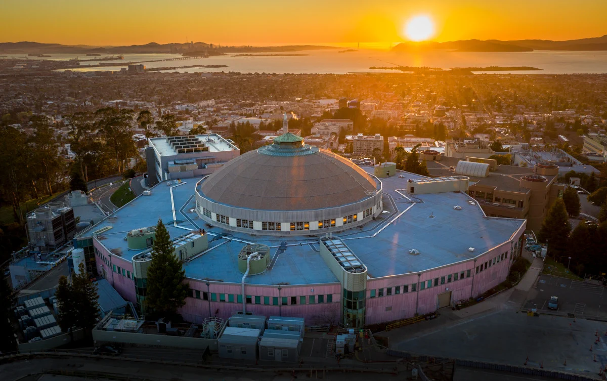 Aerial photograph of Berkeley Lab highlighting the circular Advanced Light Source, with a sunset in the background
