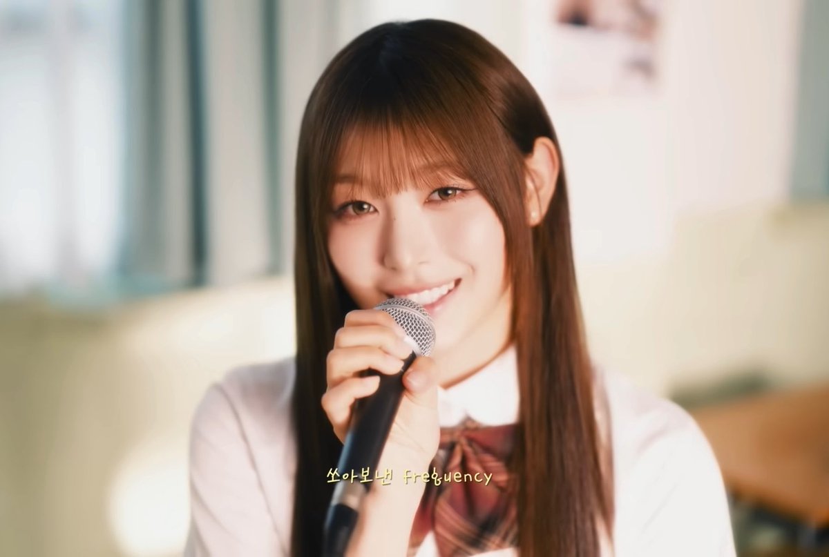 A young woman with long brown hair holds a microphone and smiles warmly, with Korean text and the English word 'frequency' overlaid on the image.