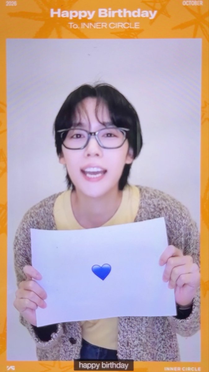 An Inner Circle birthday greeting card dated October 2026 featuring a young man with black hair and glasses holding up a white paper with a blue heart emoji, with 'Happy Birthday To. INNER CIRCLE' text at the top and 'happy birthday' caption at the bottom.