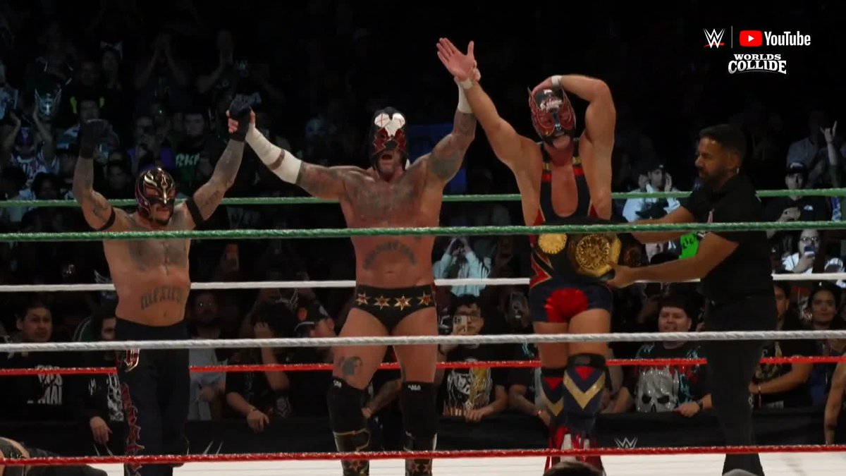 Three masked luchadors celebrate in a WWE ring with their arms raised in victory, while a referee stands nearby holding a championship belt. The "WWE YouTube Worlds Collide" logo appears in the top right corner, tying into the post's theme of uniting different generations of WWE superstars in one historic moment.