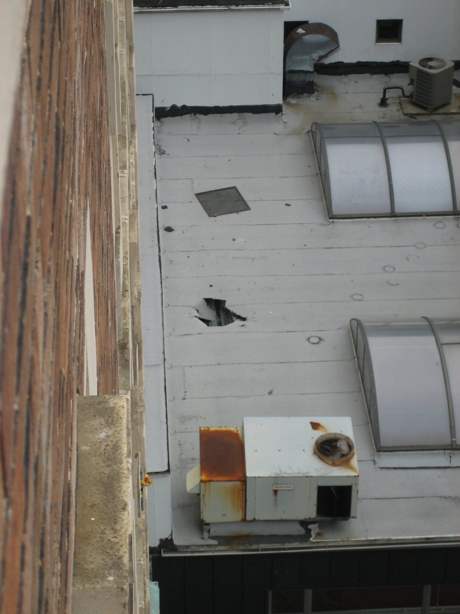 OutsidersPersp's tweet photo. Look at this angle of the breach itself.If a body hit this deck at terminal velocity from 130 feet up, basic physics dictates a high-energy, shear displacement.   Instead, look at the large, torn flap of material hanging downward. Does that look like an explosive high-velocity impact, or a material yield on a compromised, soft substrate where the decking stretched and tore under localized weight?