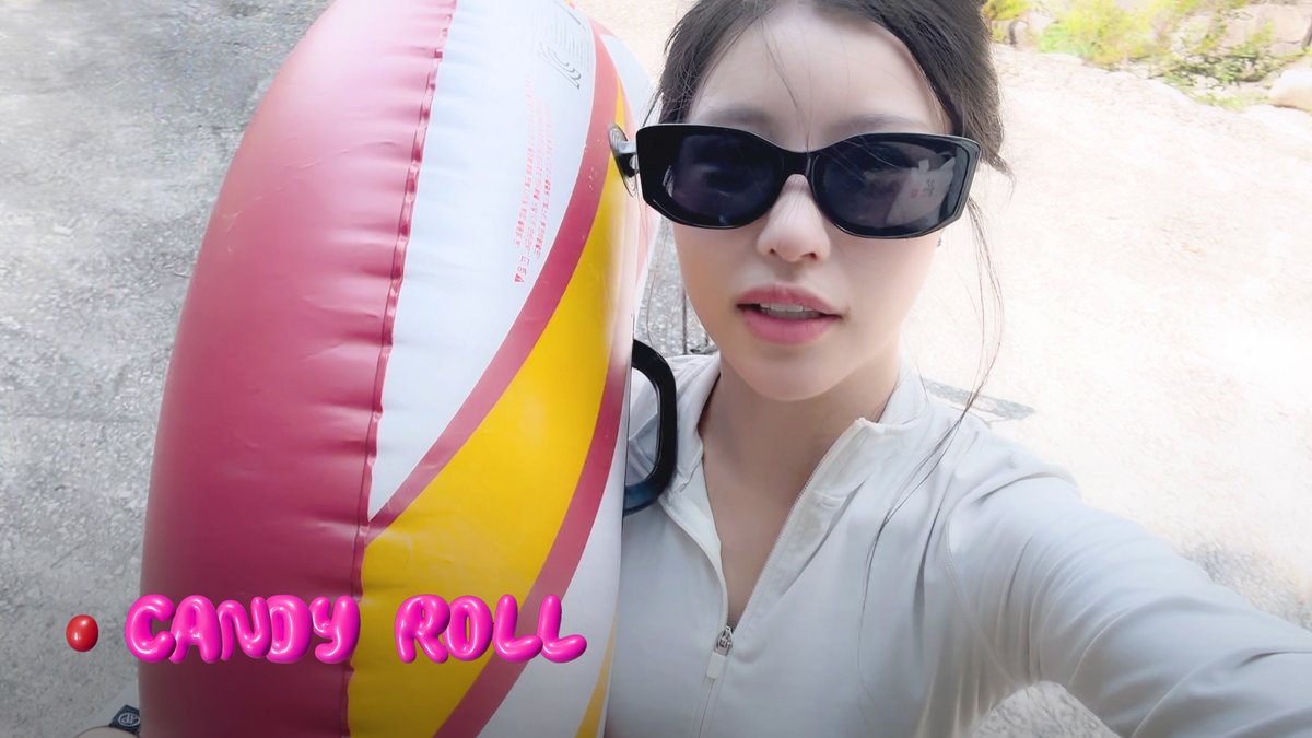 A young woman wearing black sunglasses and a white jacket poses next to a large pink and yellow inflatable candy-shaped float, with pink text reading '🍬 CANDY ROLL' overlaid on the image.