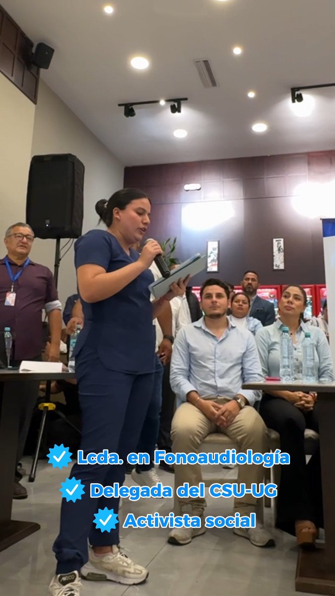 A woman in dark blue scrubs speaks into a microphone while holding a tablet at an indoor event, with text overlays identifying her as 'Lcda. en Fonoaudiología', 'Delegada del CSU-UG', and 'Activista social'.