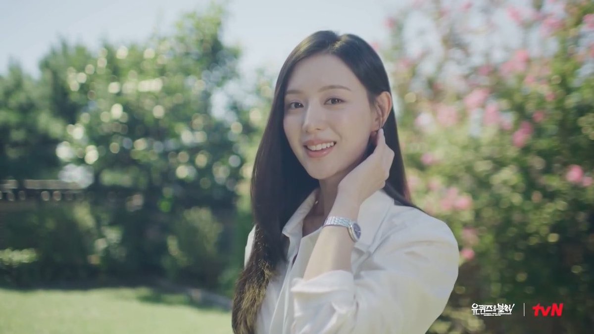 A smiling woman with long dark hair wearing a white shirt and a silver watch, standing outdoors with a tvN logo and Korean text visible in the corner.