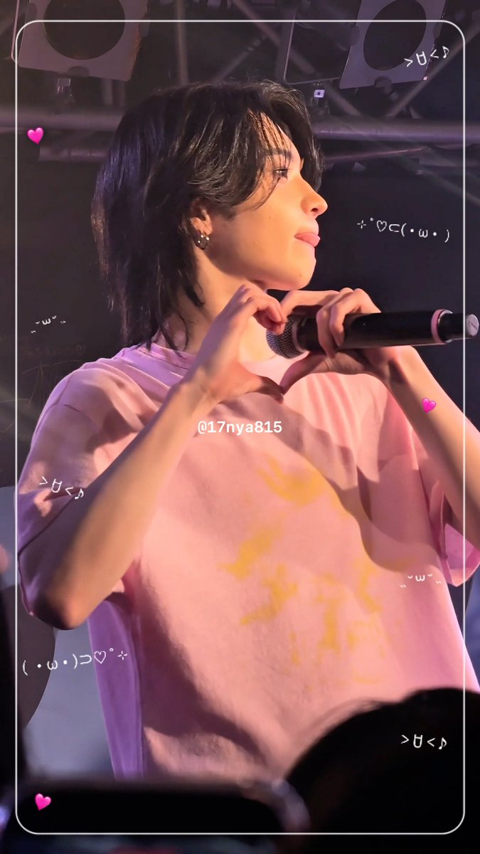 A young male performer in a pink t-shirt holds a microphone on stage, with the watermark '@17nya815' and decorative kaomoji overlays visible.