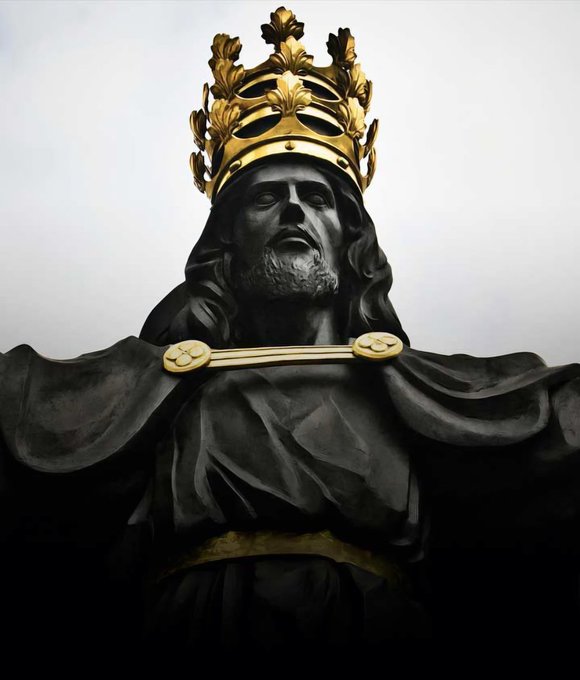 A black and gold statue depicting Jesus wearing an ornate golden crown and a cape fastened with a golden clasp.