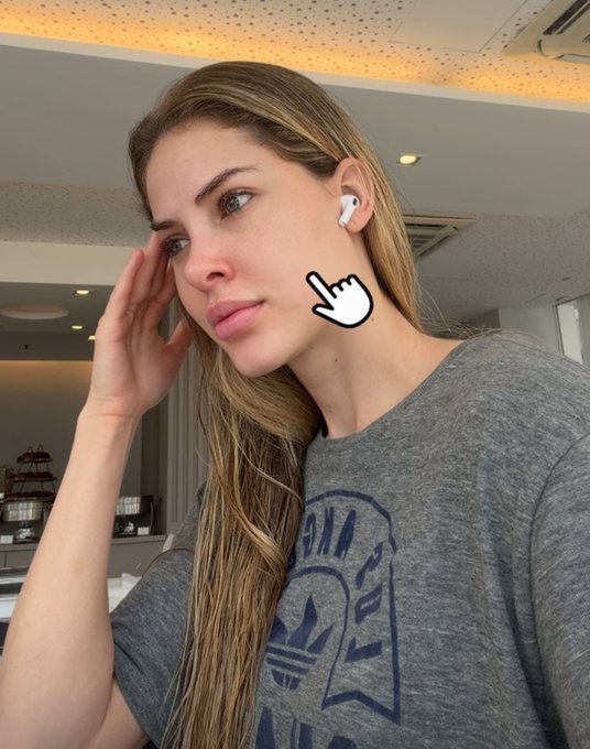 A woman wearing a gray graphic t-shirt and white earbuds poses with her hand near her face, with a cursor arrow graphic pointing to her cheek.