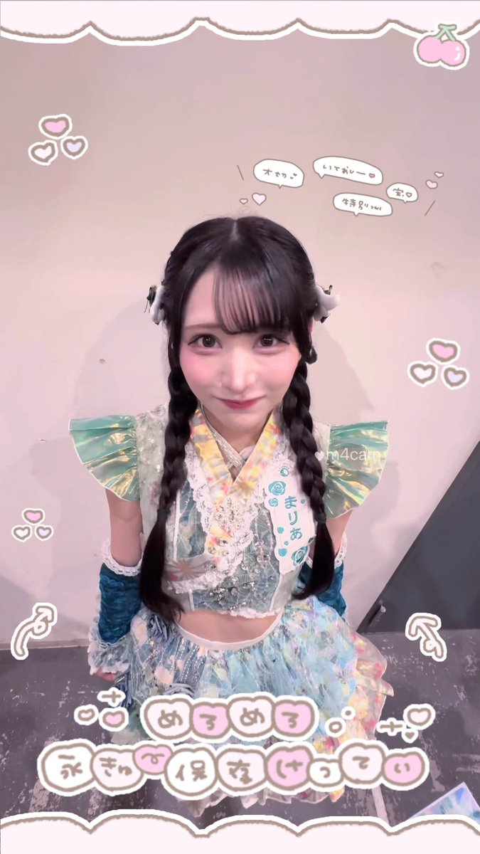 The image shows a young woman with twin braids wearing a sparkly teal and floral patterned idol outfit with a name tag reading "まりあ." The post's cute emoticon and Japanese "ニャン" (meow) sound match the playful, cat-like aesthetic, which is further emphasized by the pastel pink borders, hearts, and the on-screen text reading "めろめろ。みんな、好きになって" (Mero mero. Everyone, fall in love).