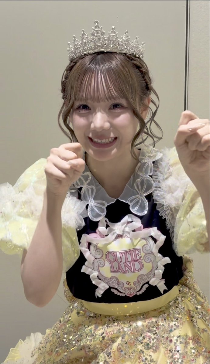 A smiling performer wearing a tiara and an ornate yellow and dark blue dress with ruffled accents poses with raised fists. The bodice displays a decorative crest reading "CUTIE LAND," matching the "#CUTIESTREET" and "#きゅーすと" (Cutie Street) hashtags from the fan-meeting post.