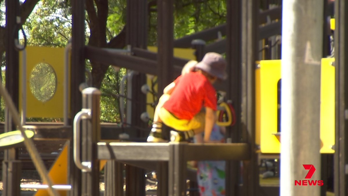 A child in a red shirt, yellow shorts, and purple hat plays on an elevated platform of a colorful playground structure, with a 7NEWS logo visible in the bottom right corner.