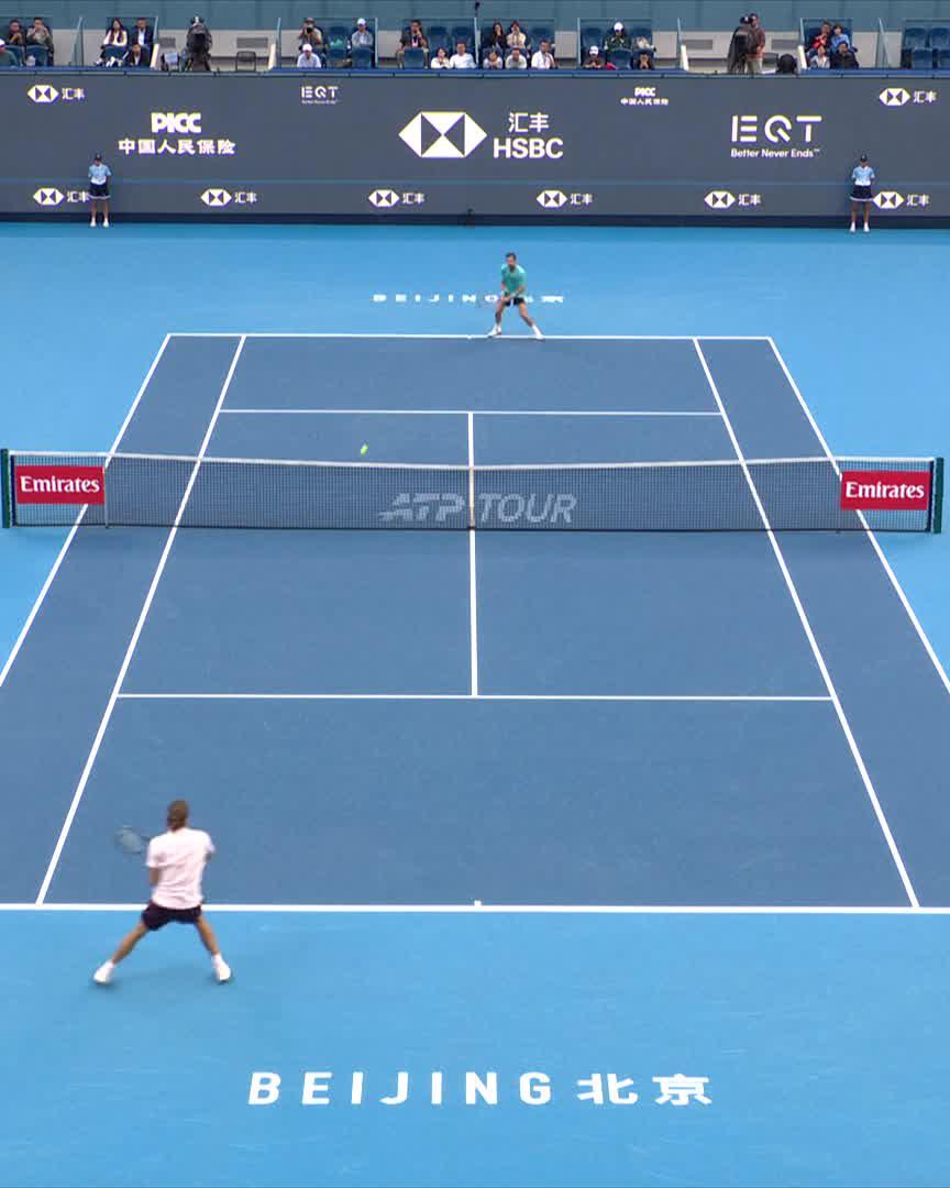 A tennis player in a white shirt prepares to return a serve during a match at the ATP Tour's China Open in Beijing, with the blue court featuring "BEIJING 北京" and sponsors HSBC, PICC, and Emirates visible on the backdrop, as the first-set tiebreak unfolds.