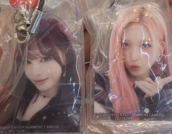 Two photocards of K-pop idols still in their original plastic packaging with metal clips; the left shows a brunette idol and the right shows an idol with pink hair, both credited to © Starship Entertainment / Amuse.