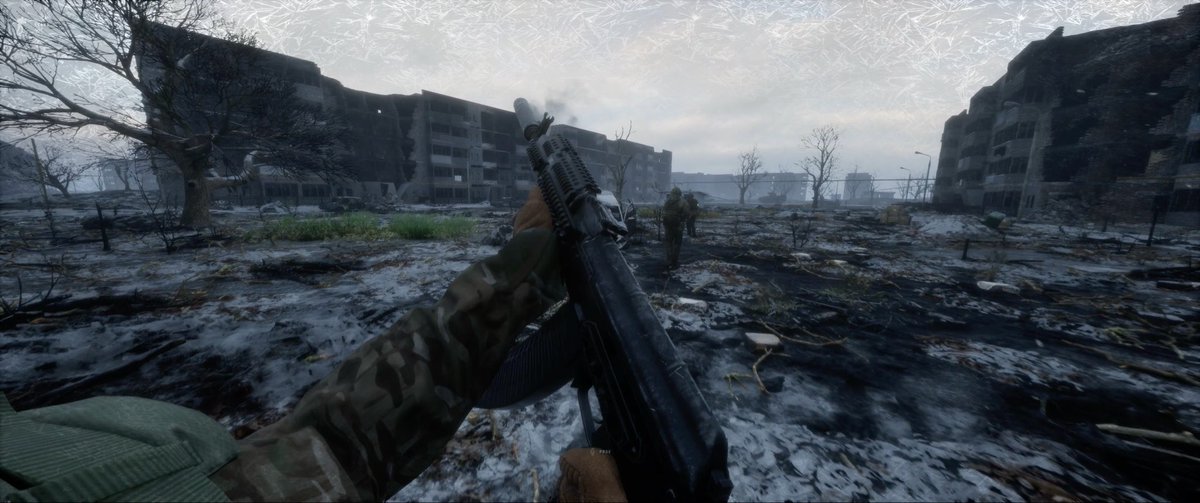 A first-person perspective screenshot from a video game showing a player holding an assault rifle in a bleak, snow-dusted, war-torn urban environment with ruined apartment buildings.